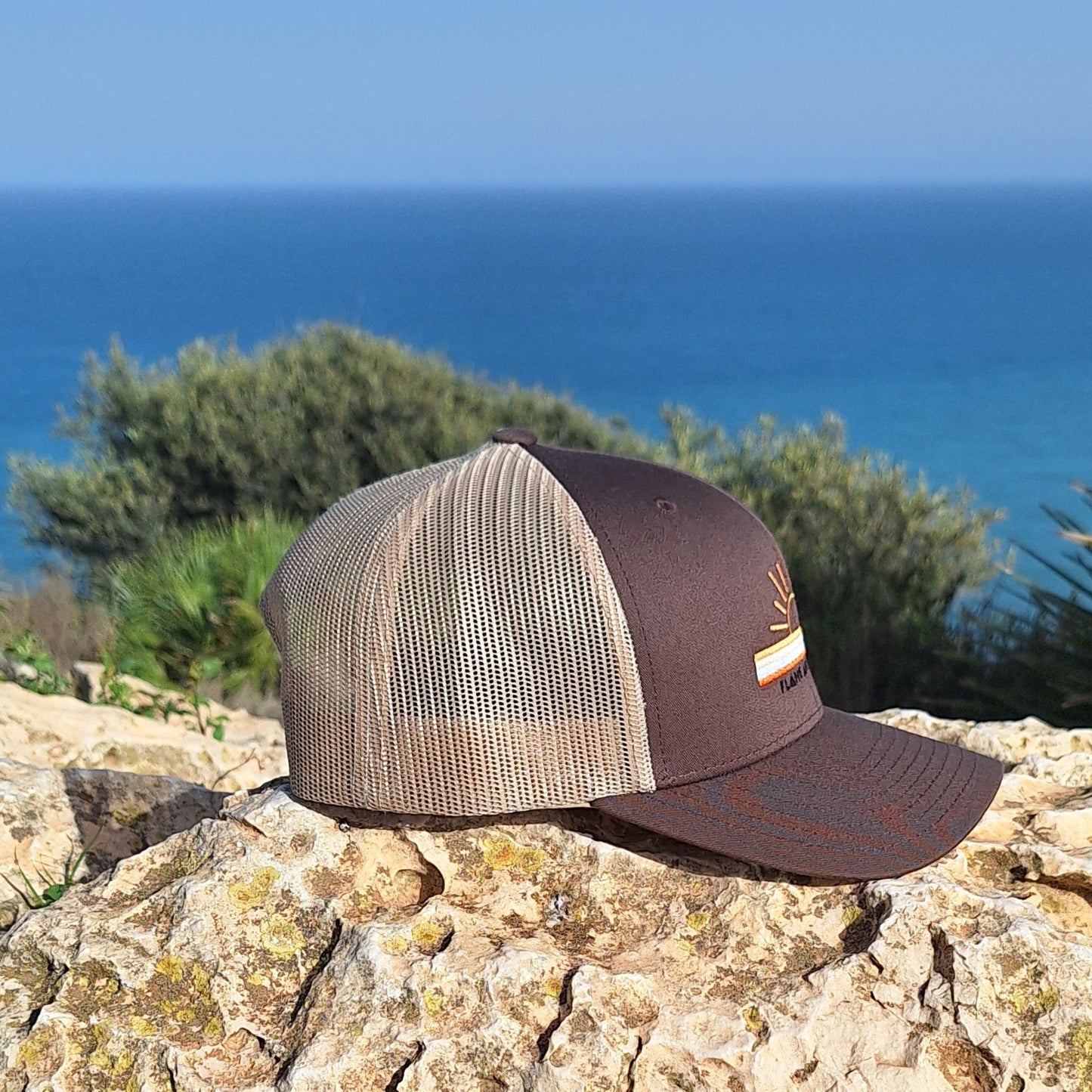 casquette trucker  non genrée, beige et marron portée par une femme avec un motif brodé soleil et bandes de couleurs ainsi que la marque flame and spirit brodée en noir