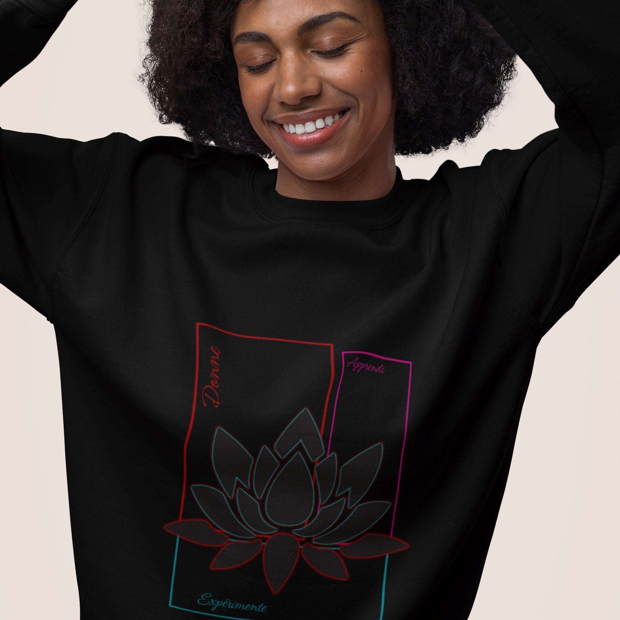 Sweat-shirt non genré, avec texte de développement personnel sur la partie ventrale, apprend, expérimente, donne, sur rectangles couleur rouge, bleu turquoise, violet, associés au symbole du lotus en transparence, fond noir. Logo brodé Flame and Spirit sous la nuque. Existe aussi en blanc.