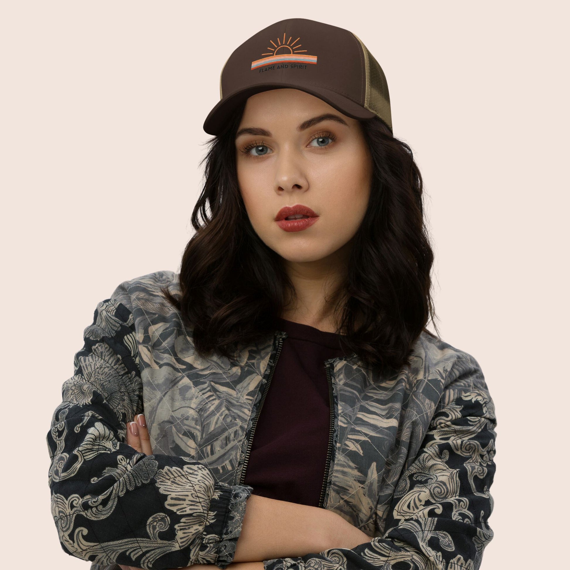 casquette trucker  non genrée, beige et marron portée par une femme avec un motif brodé soleil et bandes de couleurs ainsi que la marque flame and spirit brodée en noir