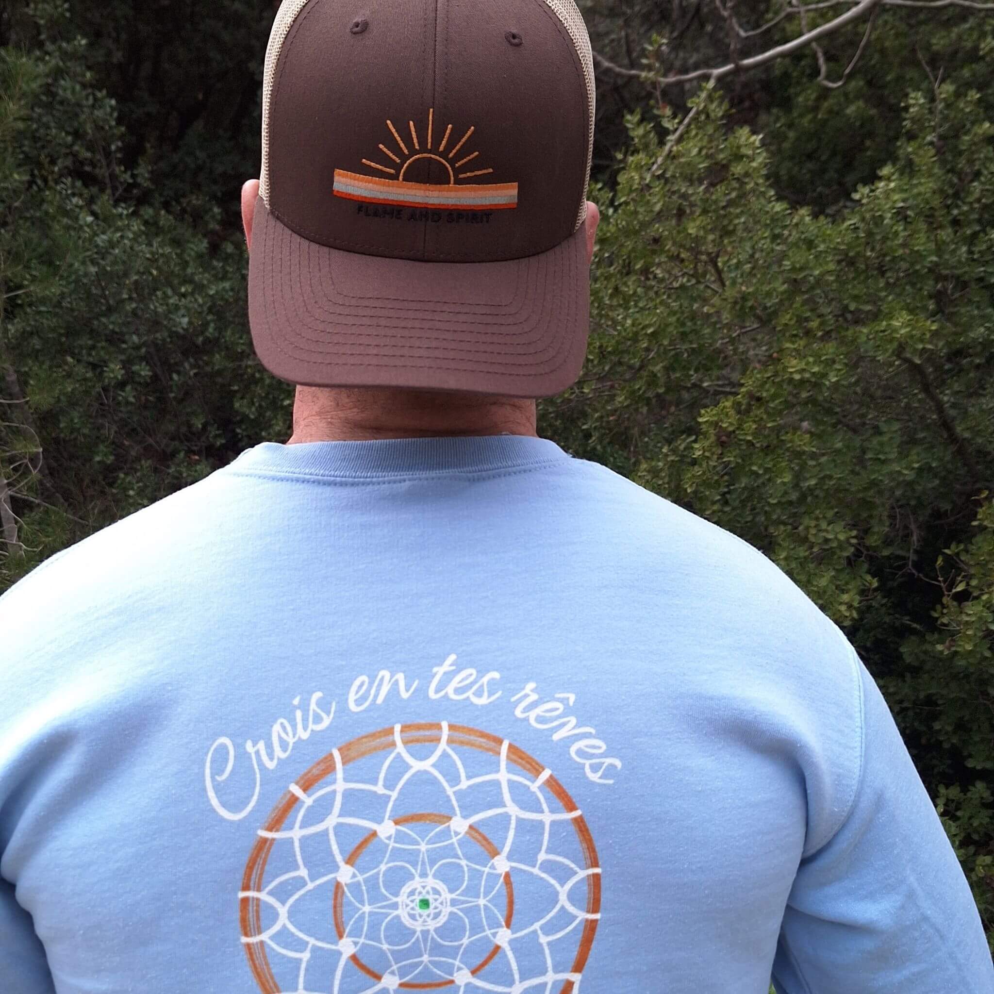 Sweat à capuche bleu clair Flame & Spirit avec motif attrape-rêve et message "Crois en tes rêves", porté avec une casquette marron.