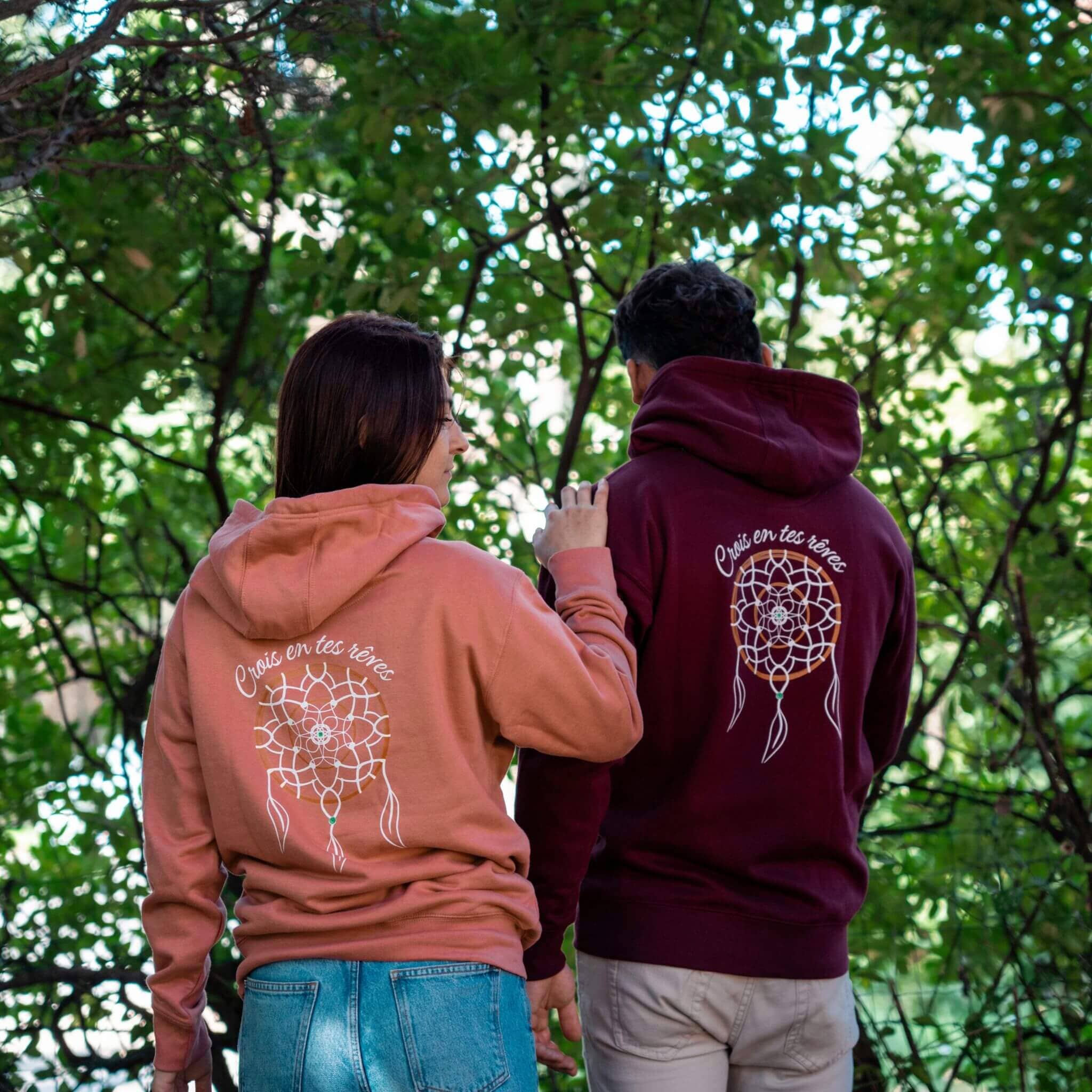 Deux personnes portent des sweats Flame & Spirit avec motif attrape-rêve et message "Crois en tes rêves", en coloris bordeaux et rose poudré.