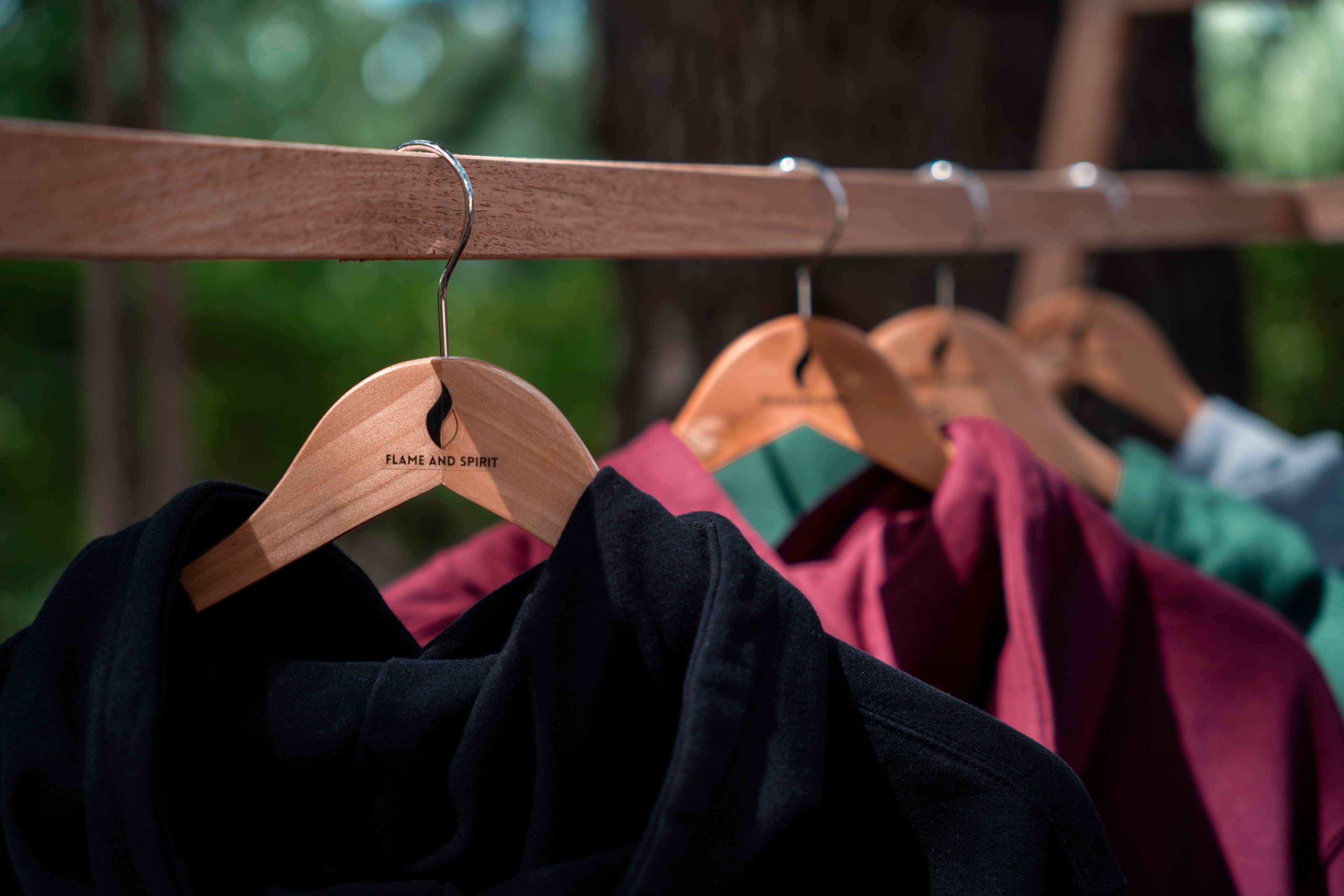 Sweats Flame & Spirit suspendus sur cintres en bois, présentant différentes couleurs et logos de la marque.