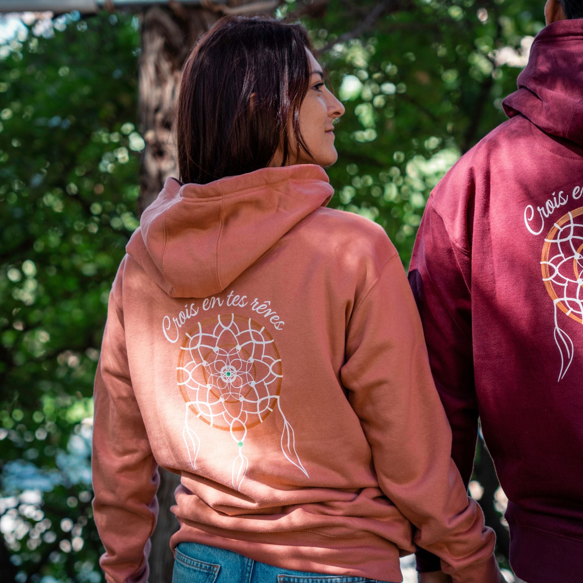 Femme portant un sweat rose Flame & Spirit avec motif attrape-rêves et message "Crois en tes rêves", en extérieur.