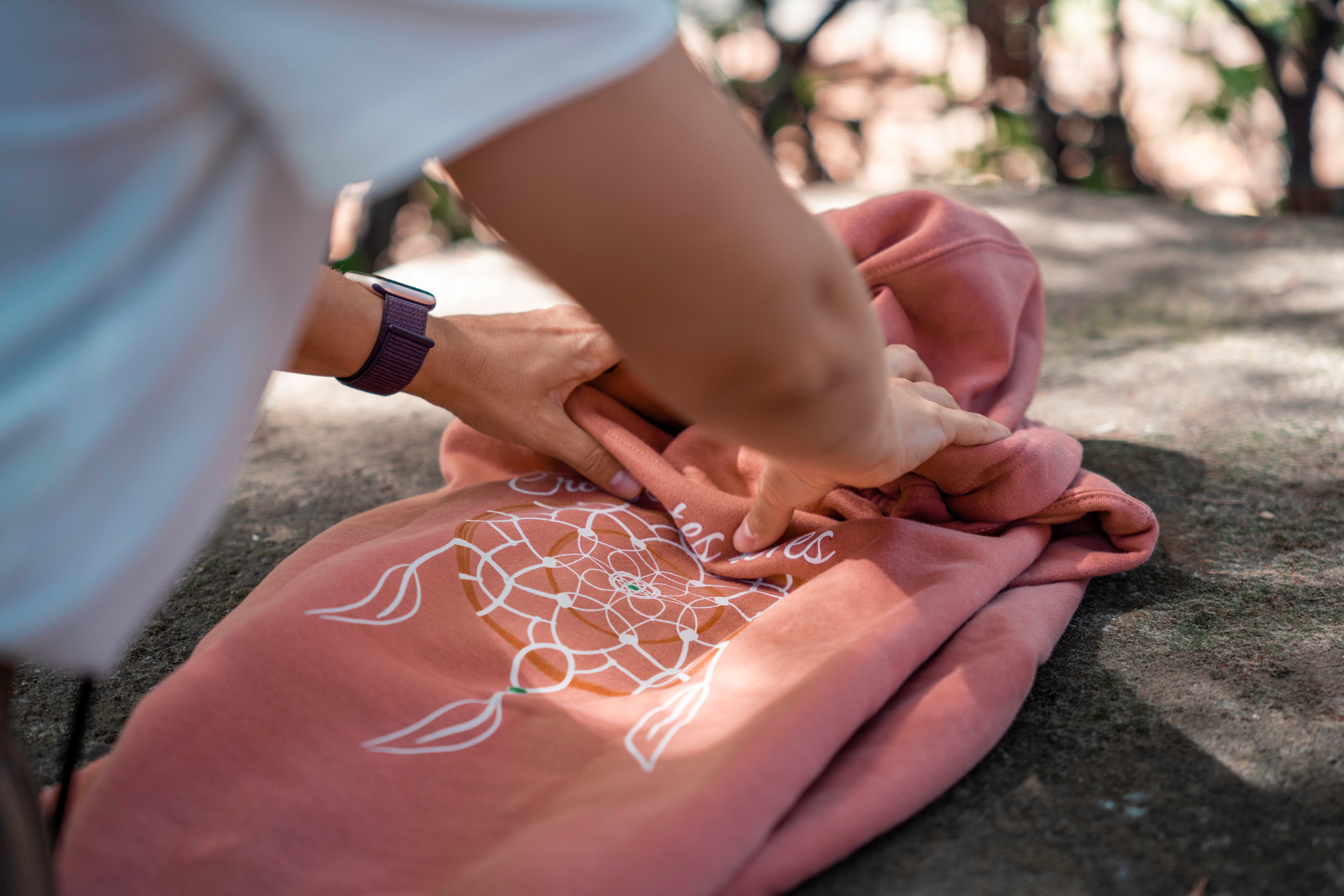 Sweat rose Flame & Spirit avec motif attrape-rêves et message “Crois en tes rêves”, déposé sur une surface naturelle.