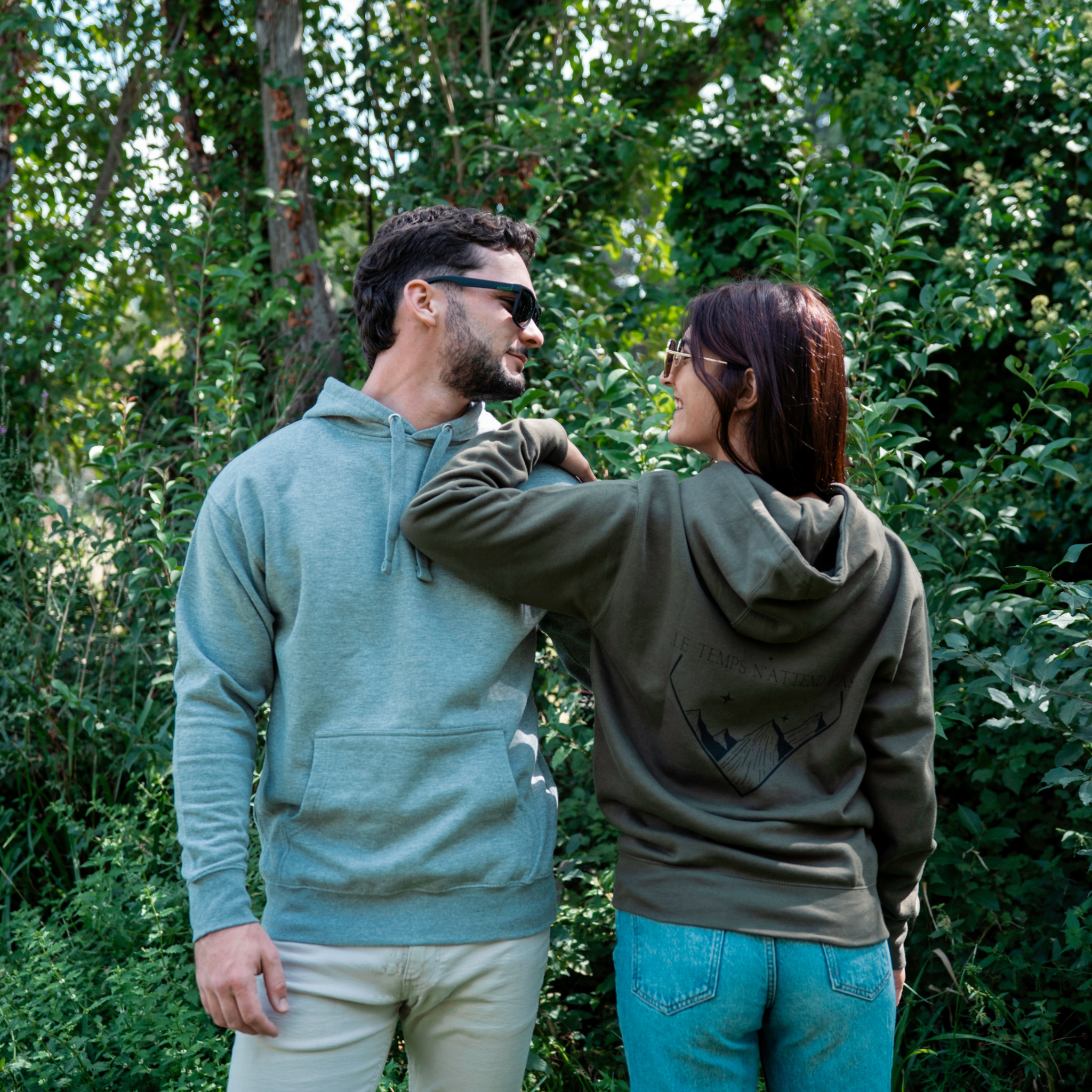 Couple portant les sweats Flame & Spirit, modèle vert avec motif montagne et message “Le temps n’attend pas”, photo prise en extérieur.