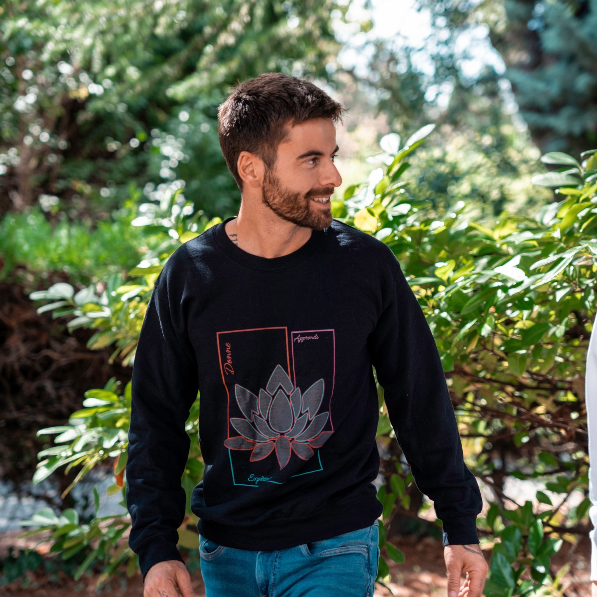 Sweat noir Flame & Spirit avec imprimé lotus coloré et message inspirant, porté en extérieur.