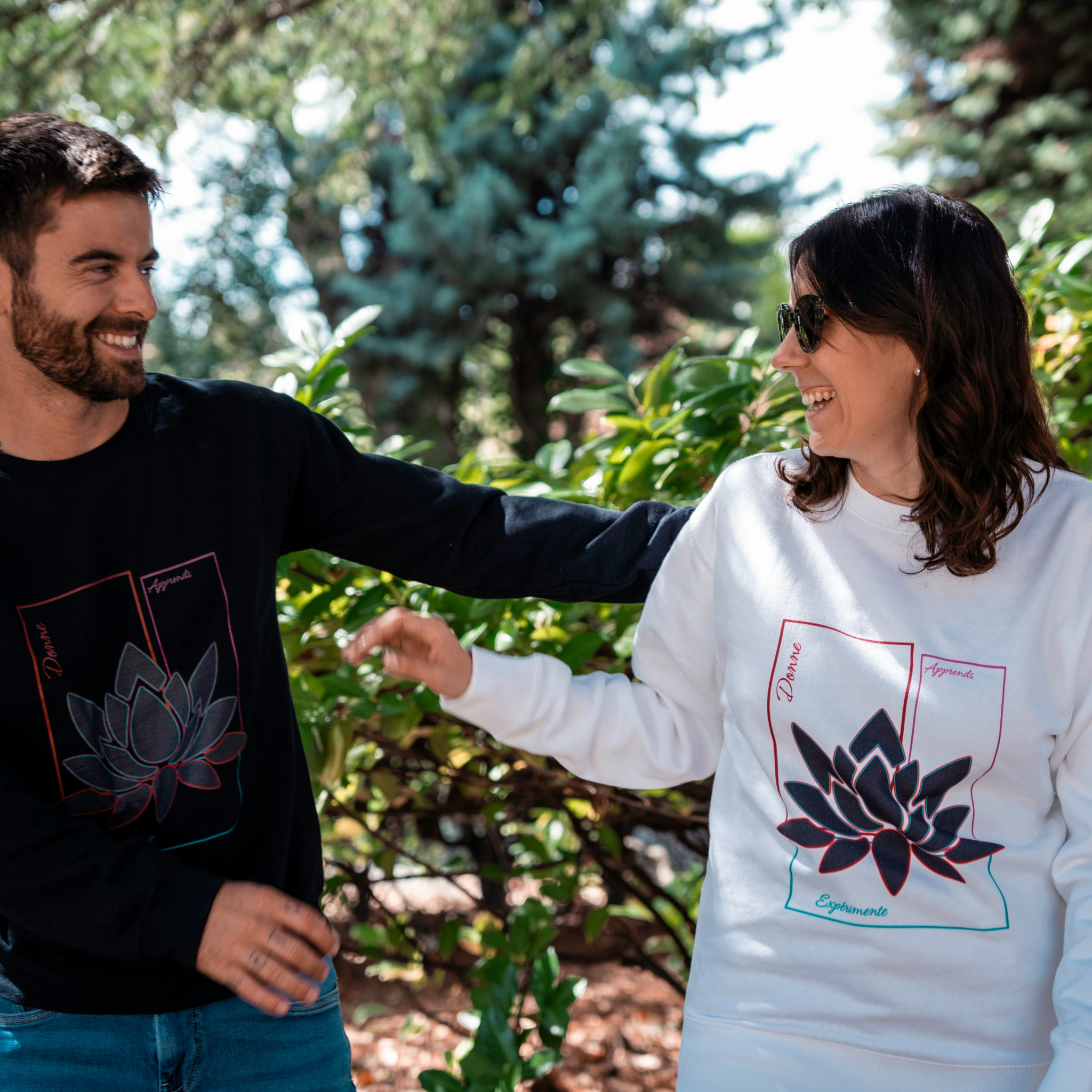 Couple portant les sweats Flame & Spirit avec motif fleur de lotus, modèles noir et blanc, photo prise en extérieur.