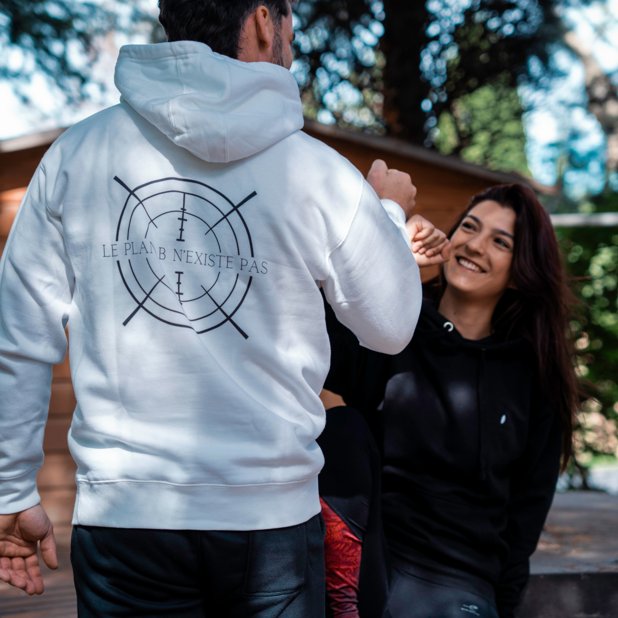 Couple portant les sweats Flame & Spirit, modèle blanc avec motif cible et message “Le plan B n’existe pas”, photo prise en extérieur.