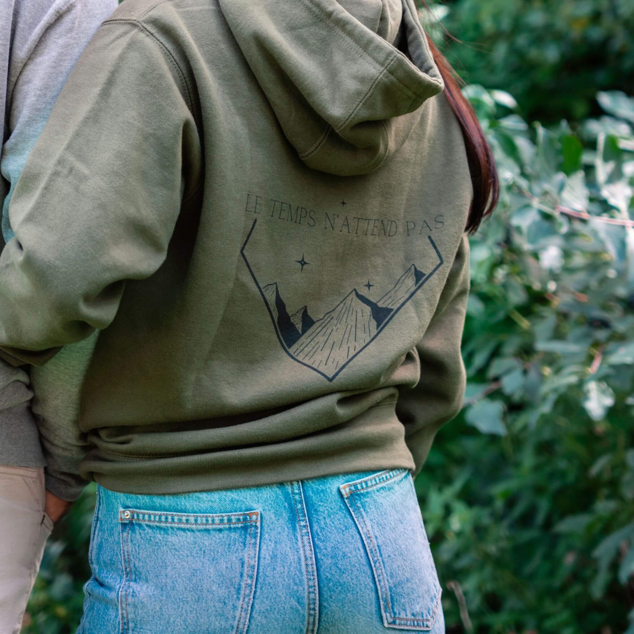 Sweat vert Flame & Spirit avec illustration de montagnes et message “Le temps n’attend pas”, vu de dos.