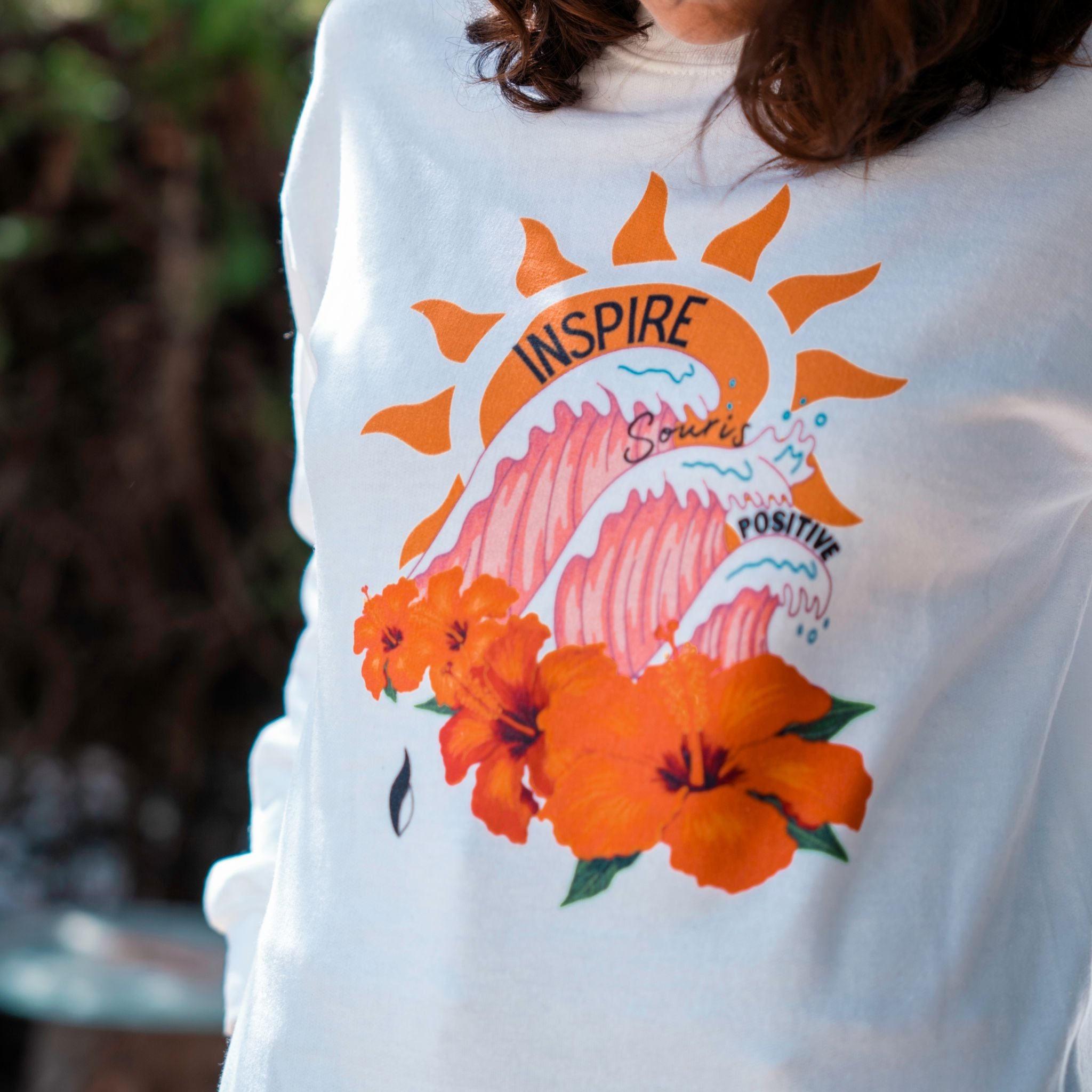 T-shirt blanc Flame & Spirit avec imprimé coloré "Inspire" représentant un soleil, des vagues et des fleurs orange.